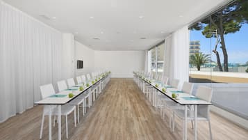 A conference room with a long table, white chairs, and a view of the sea through large windows.