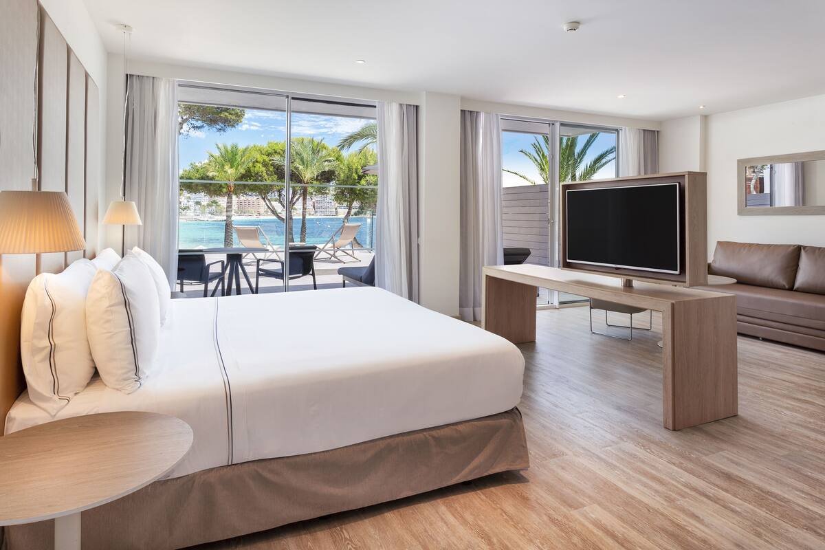 Habitación de hotel moderna con una cama grande, un escritorio con televisor de pantalla plana, un sofá y un balcón con vista a la piscina.