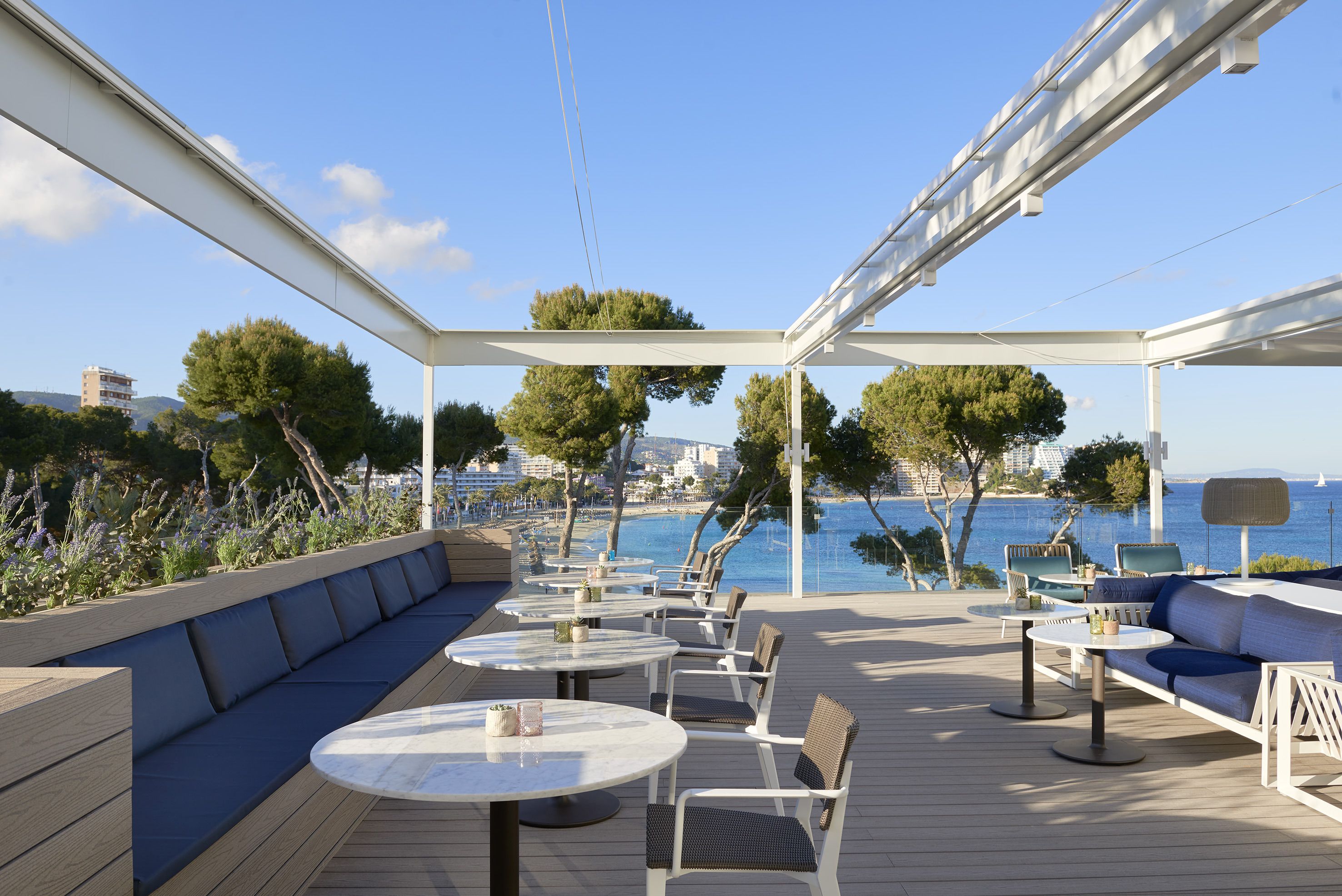 An outdoor deck with seating and tables, overlooking a body of water and cityscape.