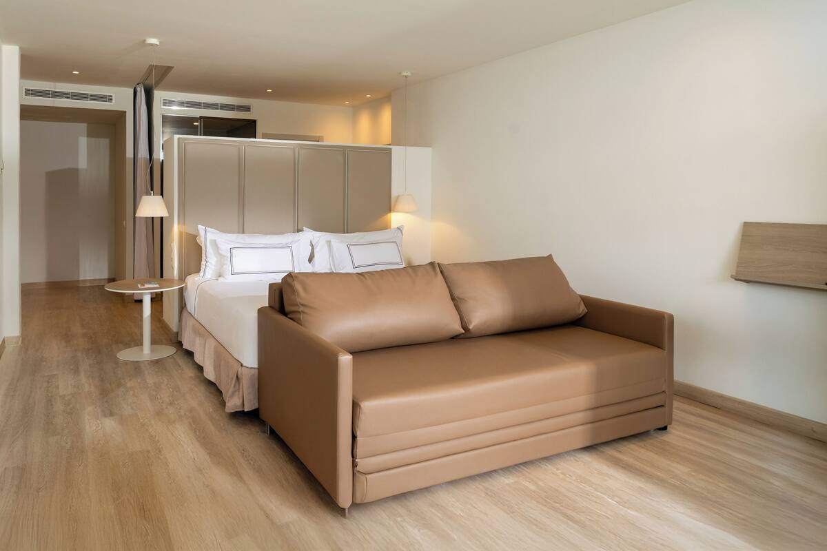 Una habitación de hotel moderna con una cama grande, un sofá, una mesita redonda y una lámpara.