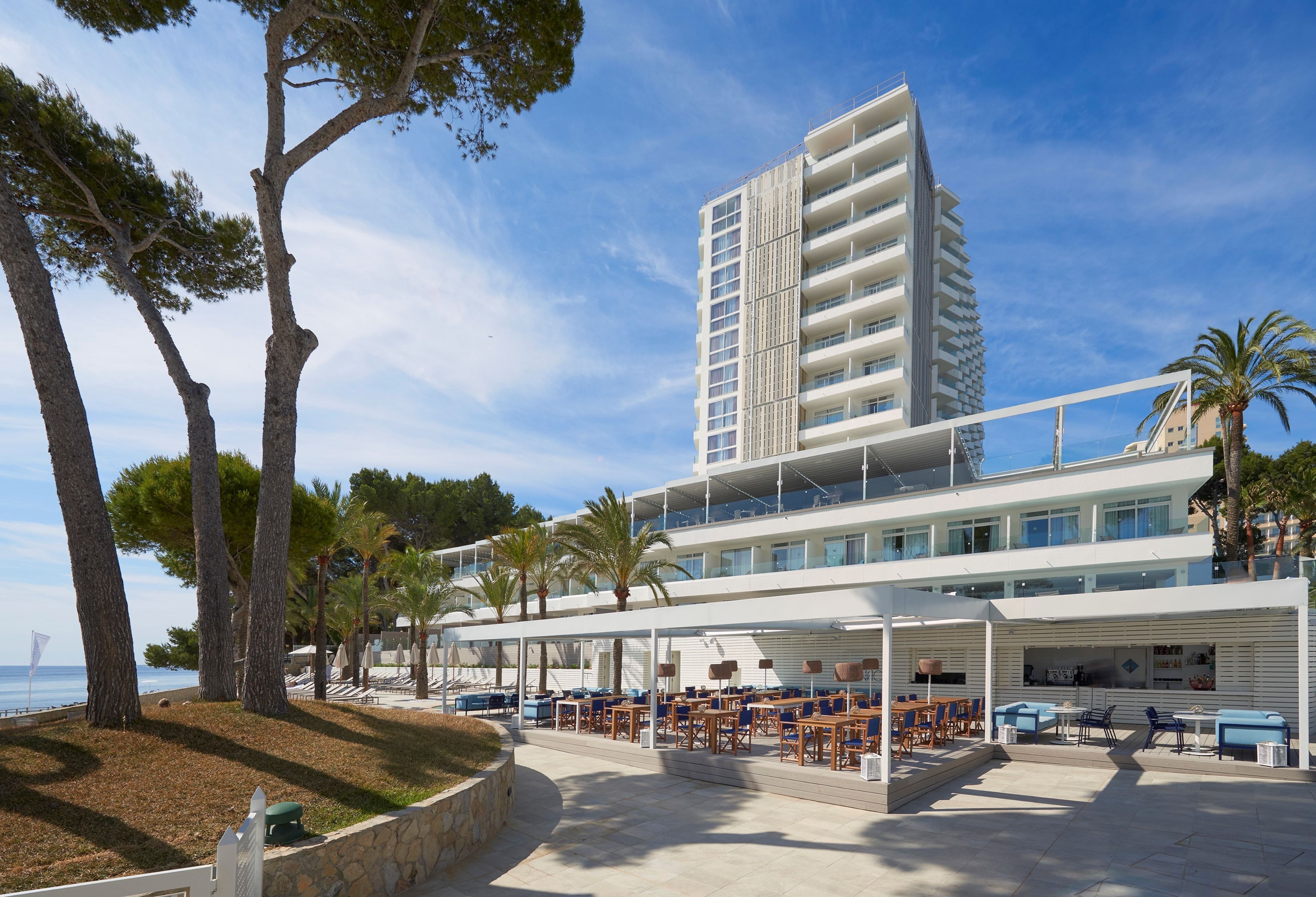 A modern hotel with a terrace overlooking the sea, featuring outdoor seating and a view of the ocean.