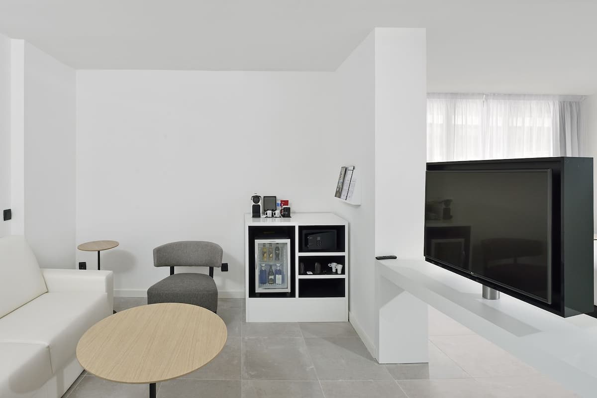 Uma sala de estar moderna e minimalista com uma televisão de tela plana grande, um sofá branco, uma mesa de centro redonda e uma pequena mesa lateral.