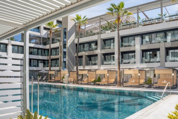 A modern hotel with a pool, lounge chairs, and palm trees.