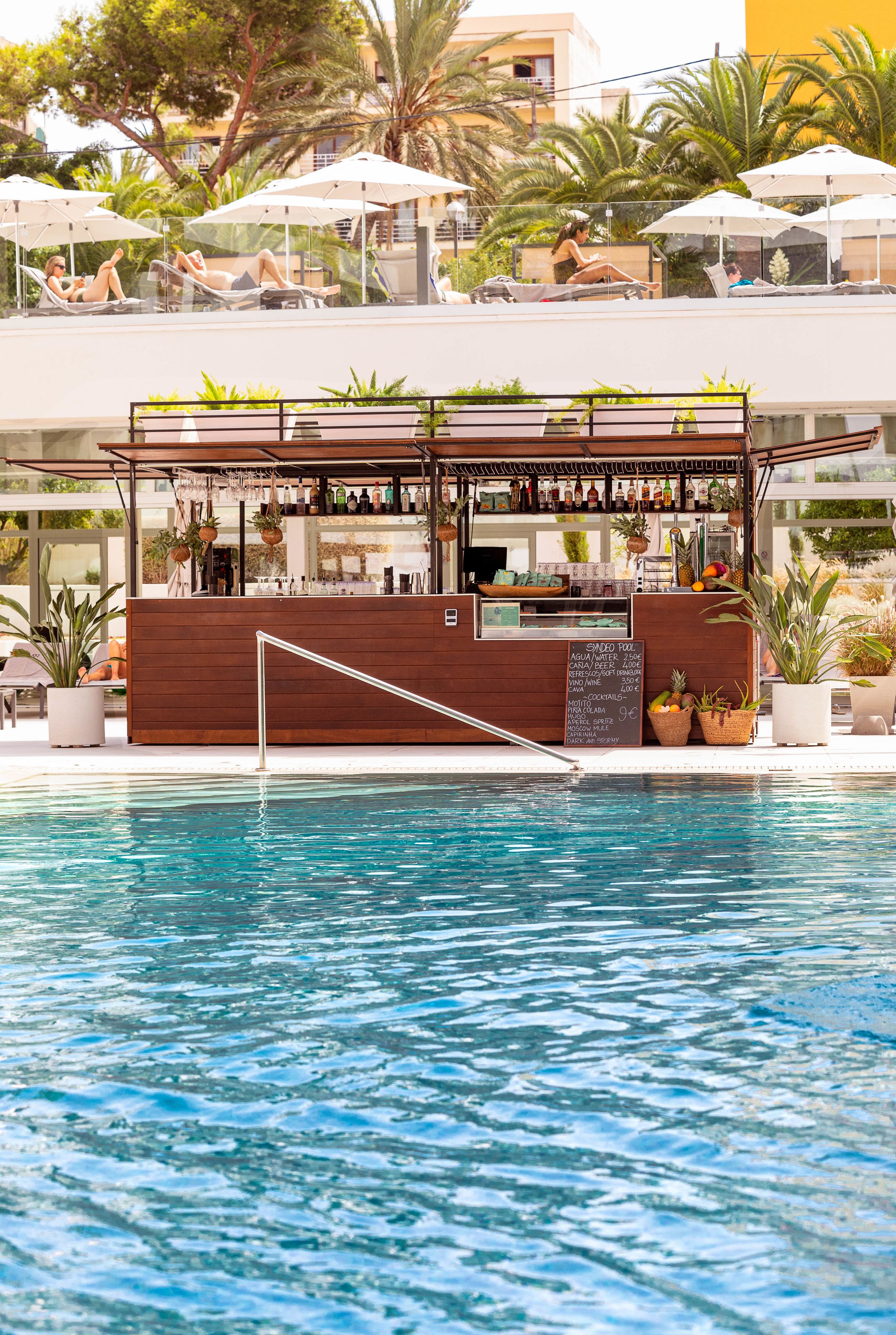 Un bar junto a la piscina con mostrador de madera, taburetes y sombrillas.