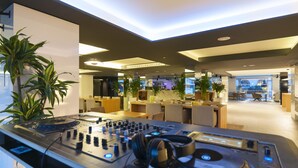 A modern lobby with a DJ setup, seating areas, and indoor plants.