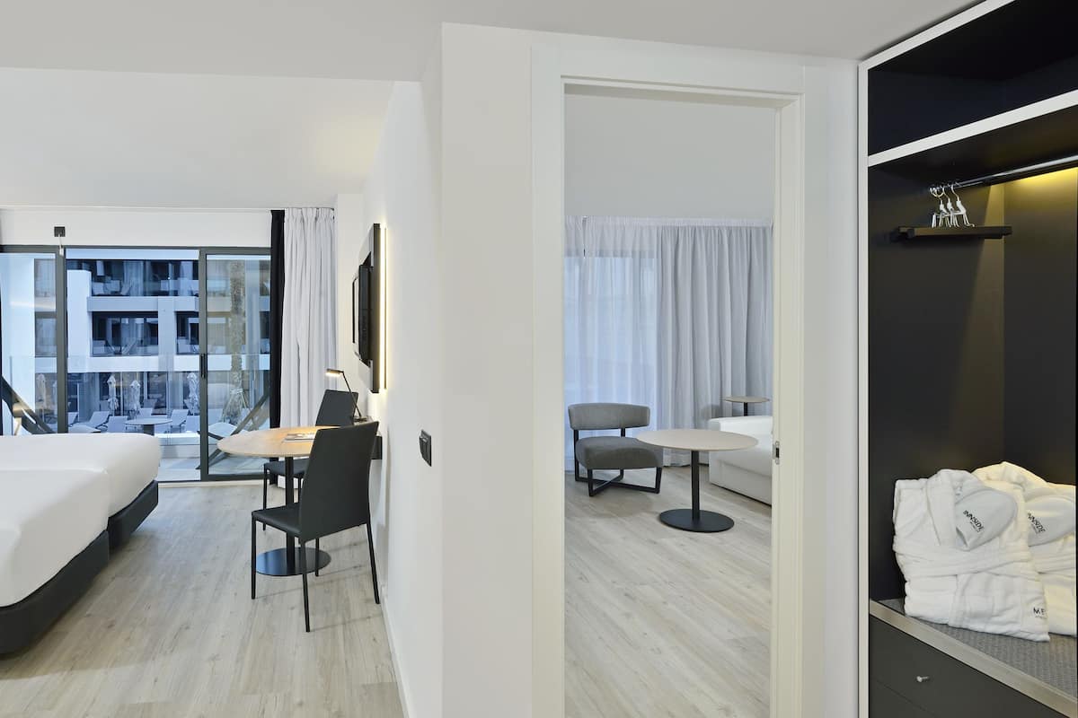 Quarto de hotel moderno com uma cama grande, uma escrivaninha, uma cadeira e varanda com vista para a cidade.