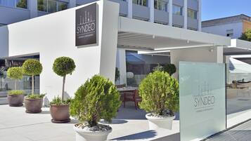 Un espace SYNDEO comprenant un salon et un restaurant avec des places assises en plein air, des plantes en pot et un design architectural moderne.