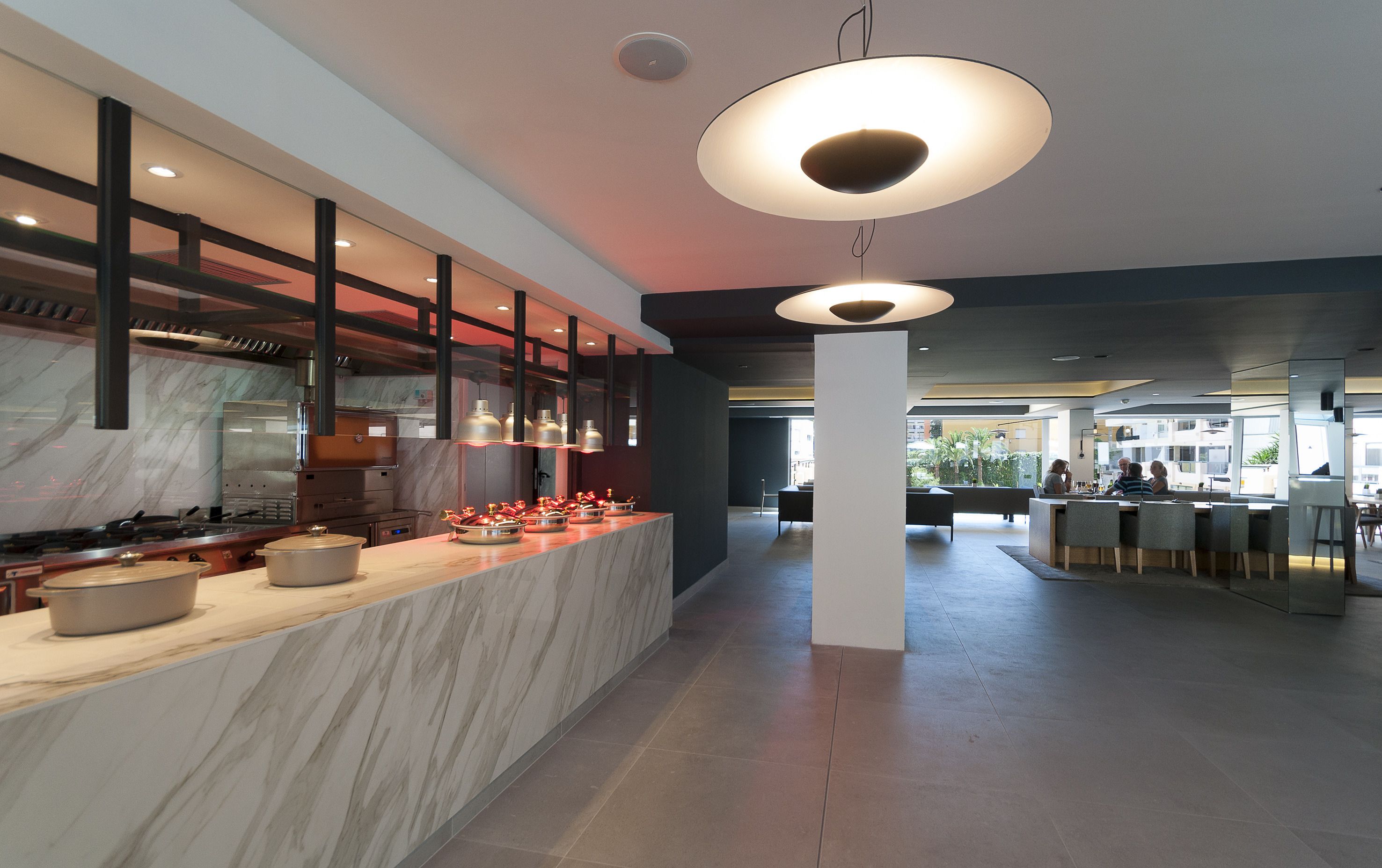 A modern kitchen with a marble countertop, overhead lighting, and a view into the dining area.