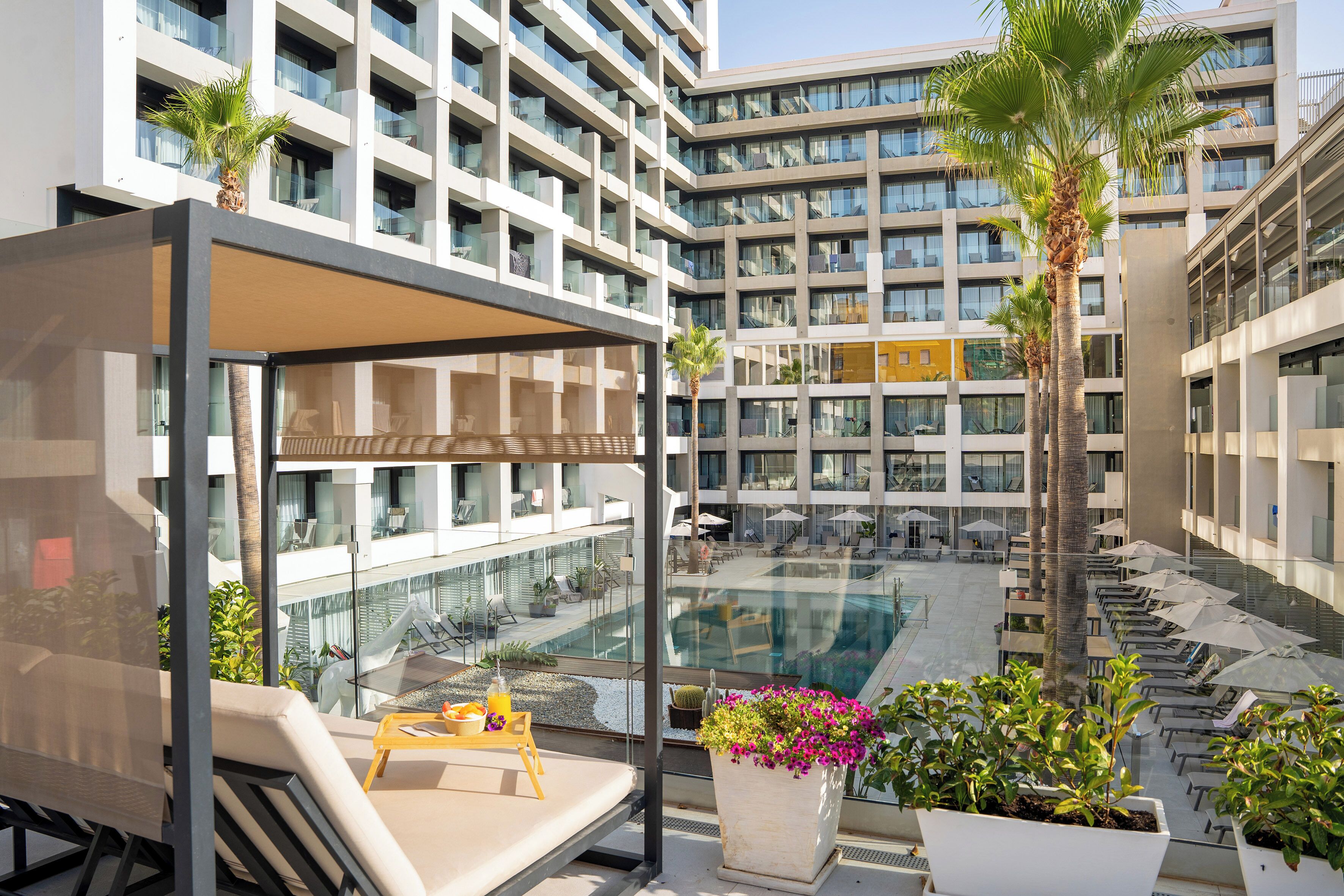 A modern hotel courtyard with a pool, lounge chairs, and potted plants.