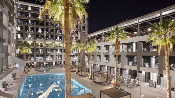 A hotel with a large indoor pool, multiple floors, and palm trees.