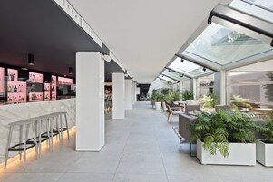 Un moderno vestíbulo de hotel con una zona de bar, asientos y plantas en macetas.