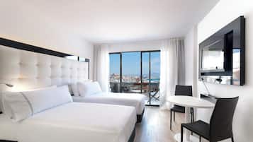 A hotel room with two beds, a TV, a dining table with chairs, and a view of a cityscape.