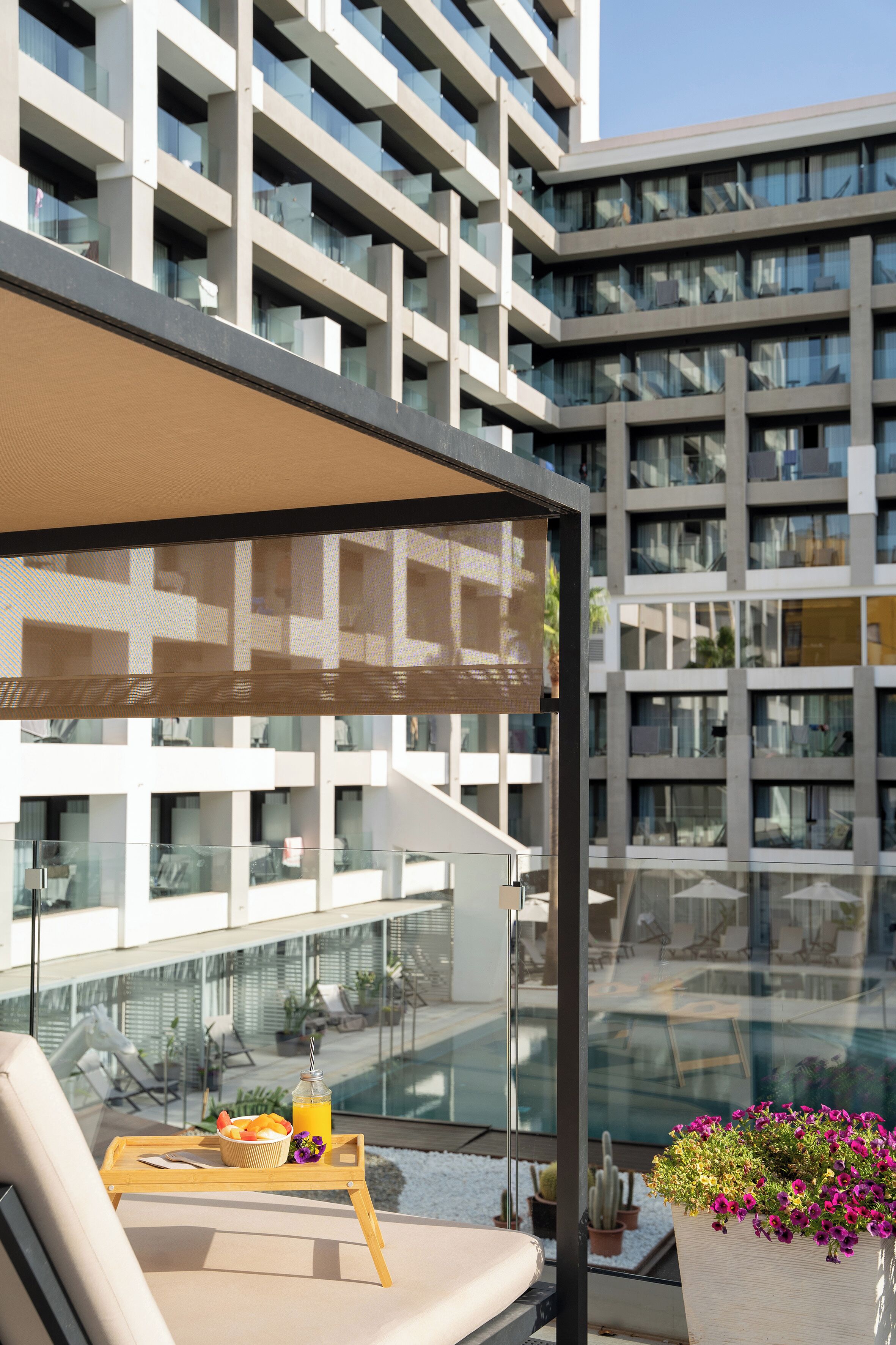 Un balcon avec une table en verre, une chaise et un plateau contenant des fruits et une boisson.
