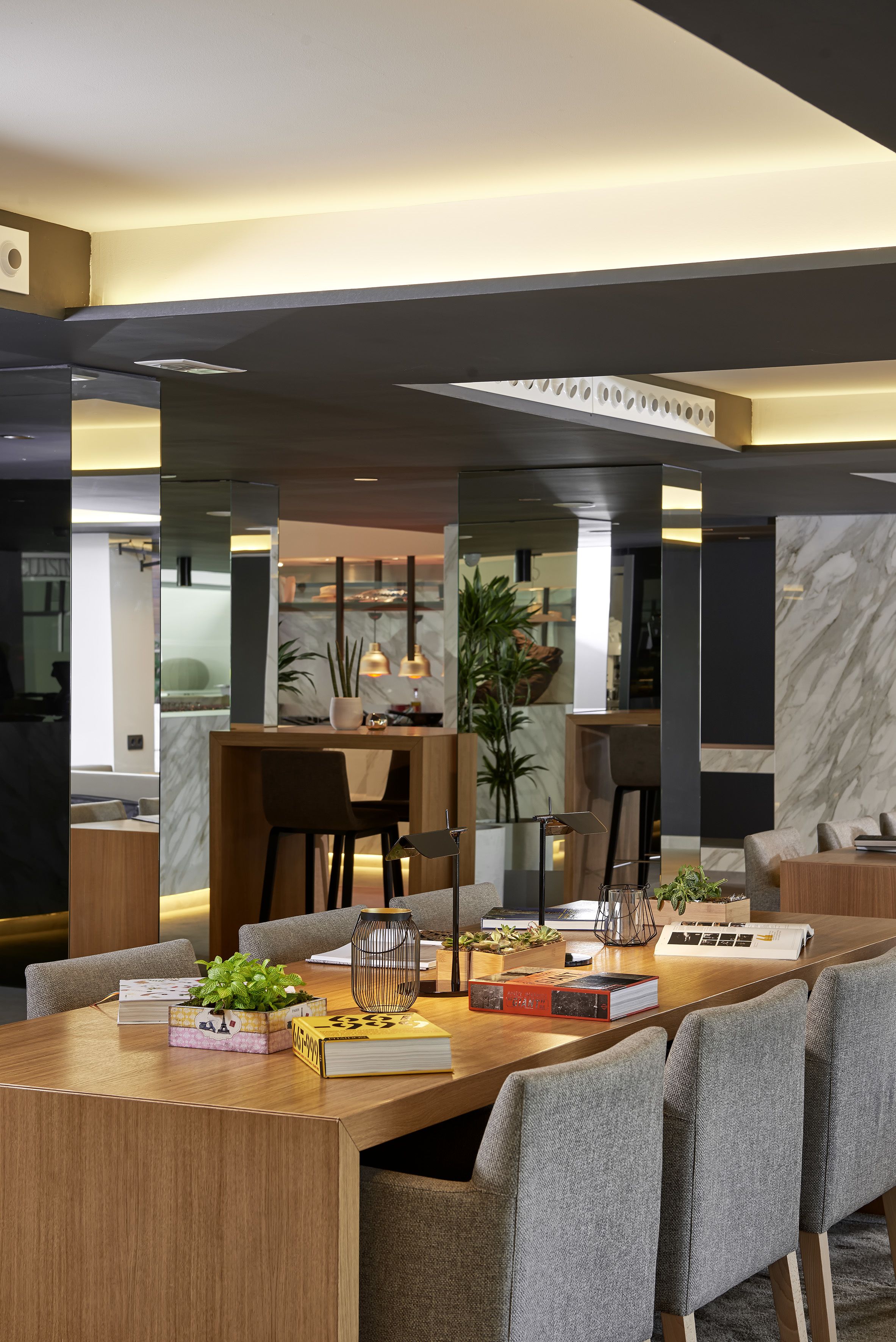 A modern dining area with a wooden table, grey upholstered chairs, and a marble wall in the background.