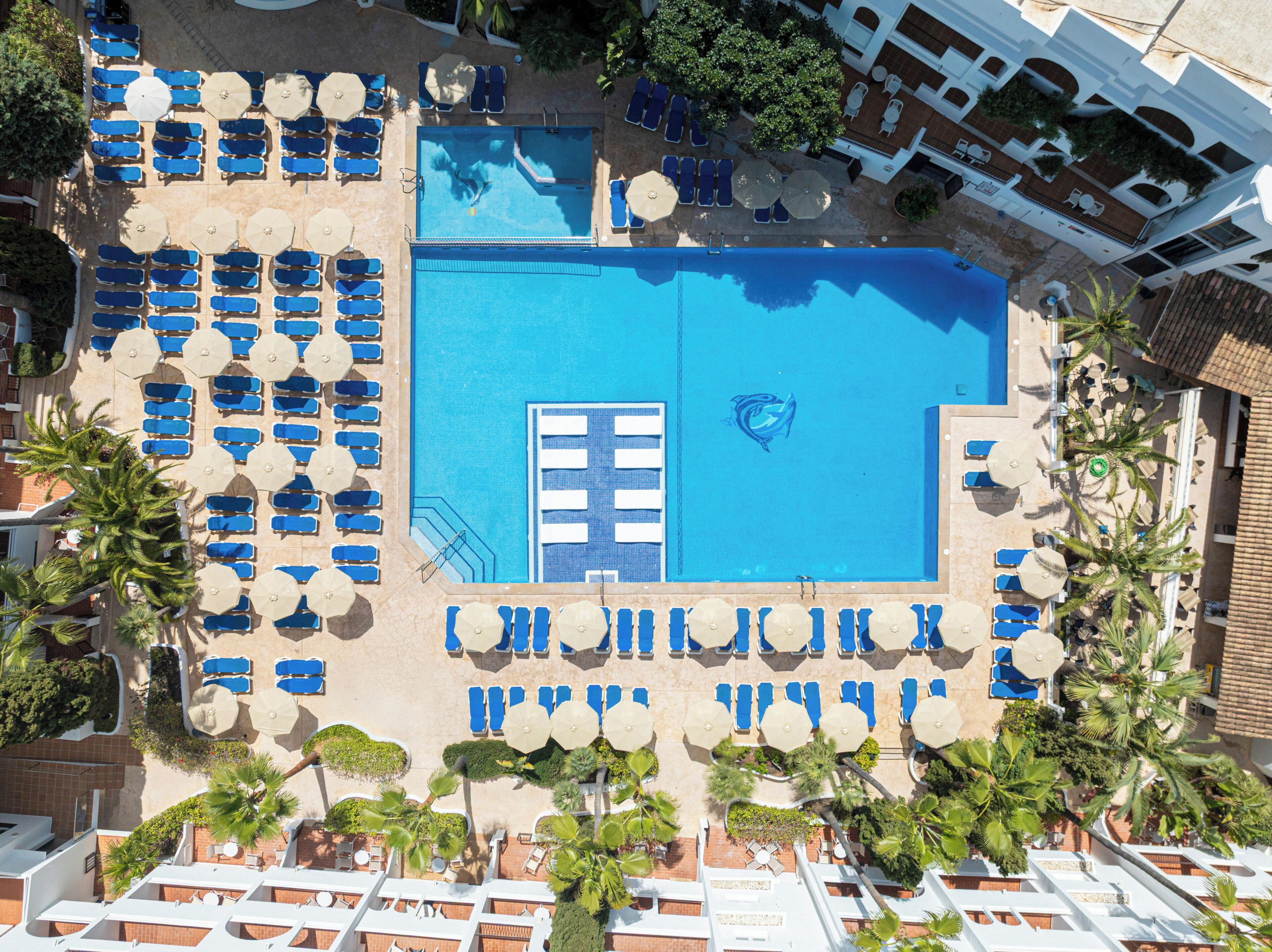 An aerial view of a resort with multiple swimming pools, sun loungers, and palm trees.