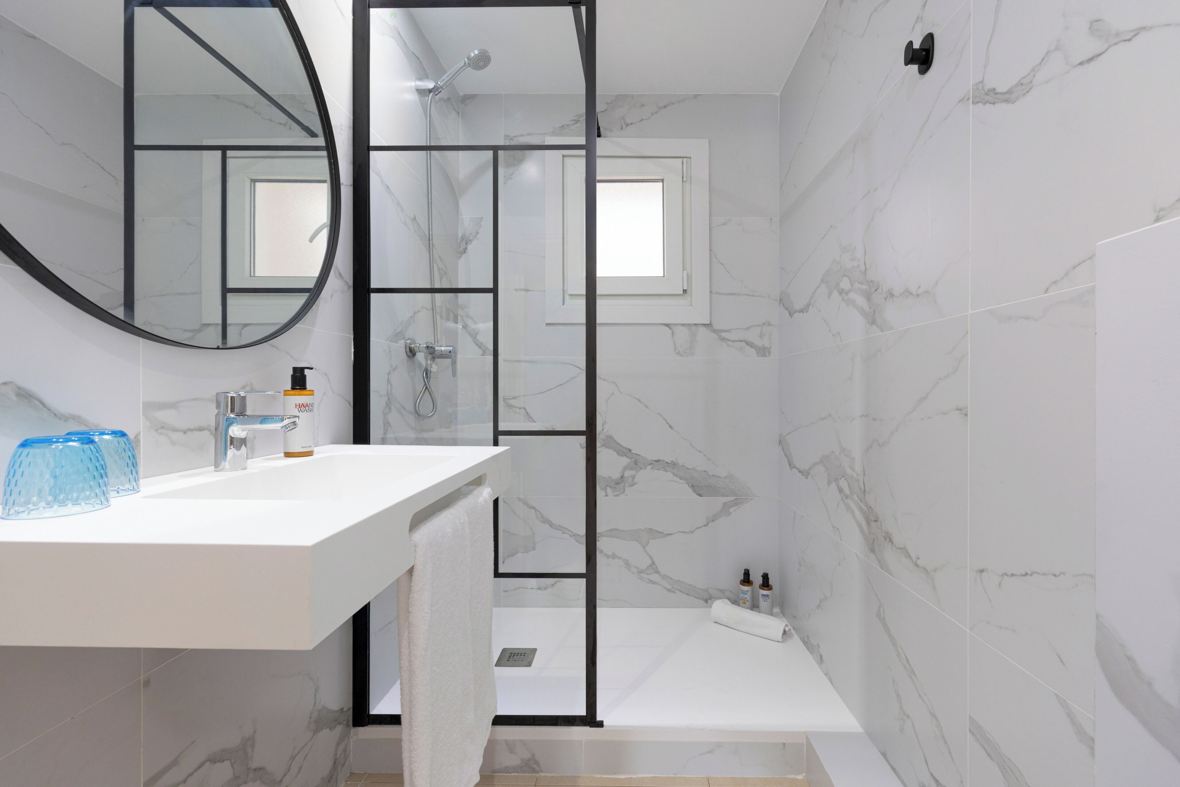 Une salle de bain moderne avec une douche à parois de verre, un lavabo blanc avec un miroir et des murs en marbre.