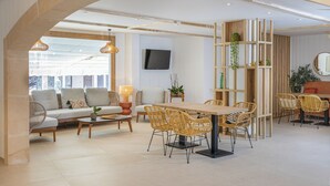 Un vaste espace de vie comprenant un canapé, une table basse et une table à manger avec des chaises. Un téléviseur est fixé au mur, et l’on y trouve également des plantes et une bibliothèque.