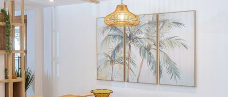 Et spiseområde med et træbord og stole, en hængende lampe samt et billede af palmer på væggen.