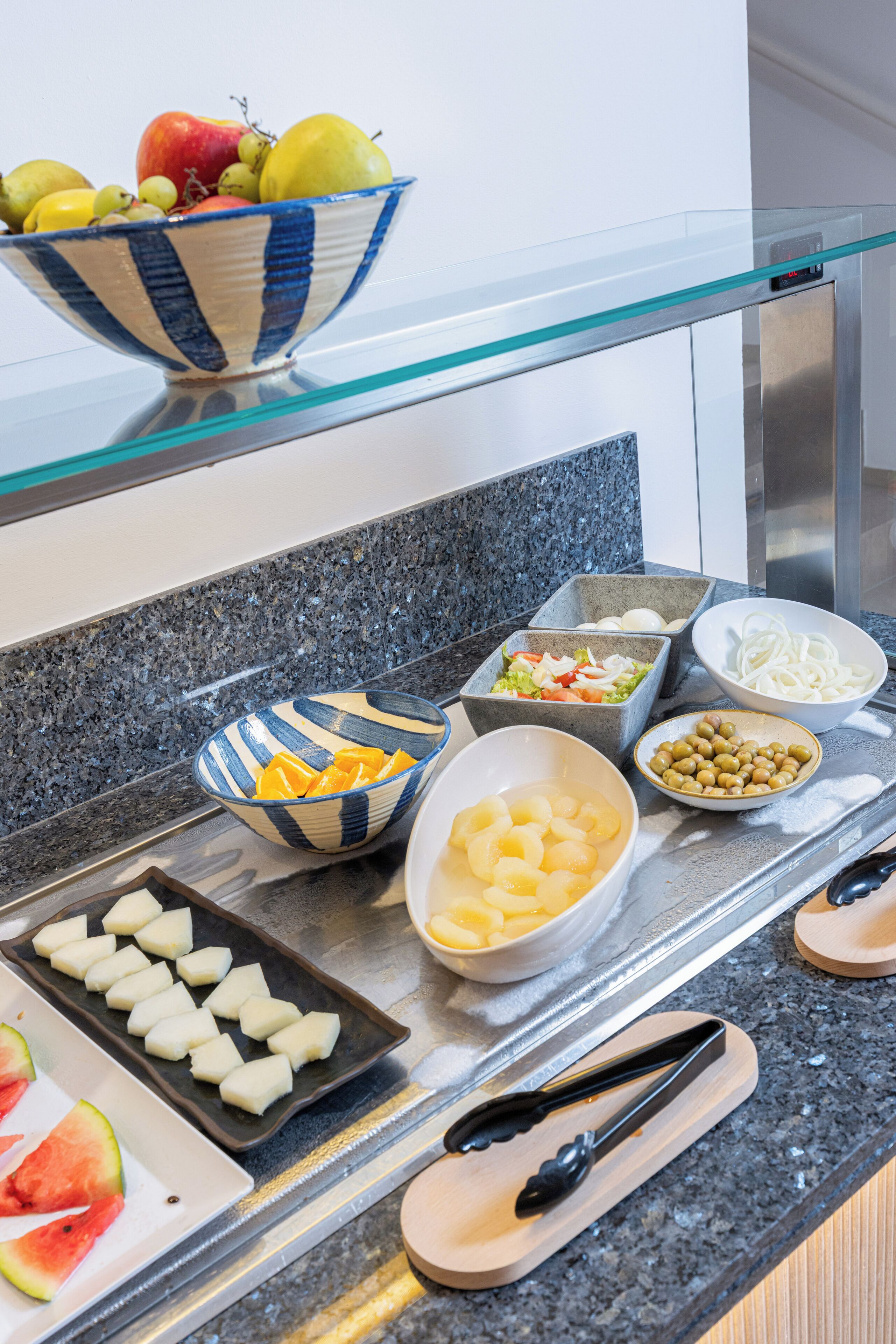 A kitchen counter with various bowls containing fruits, vegetables, and sliced potatoes.
