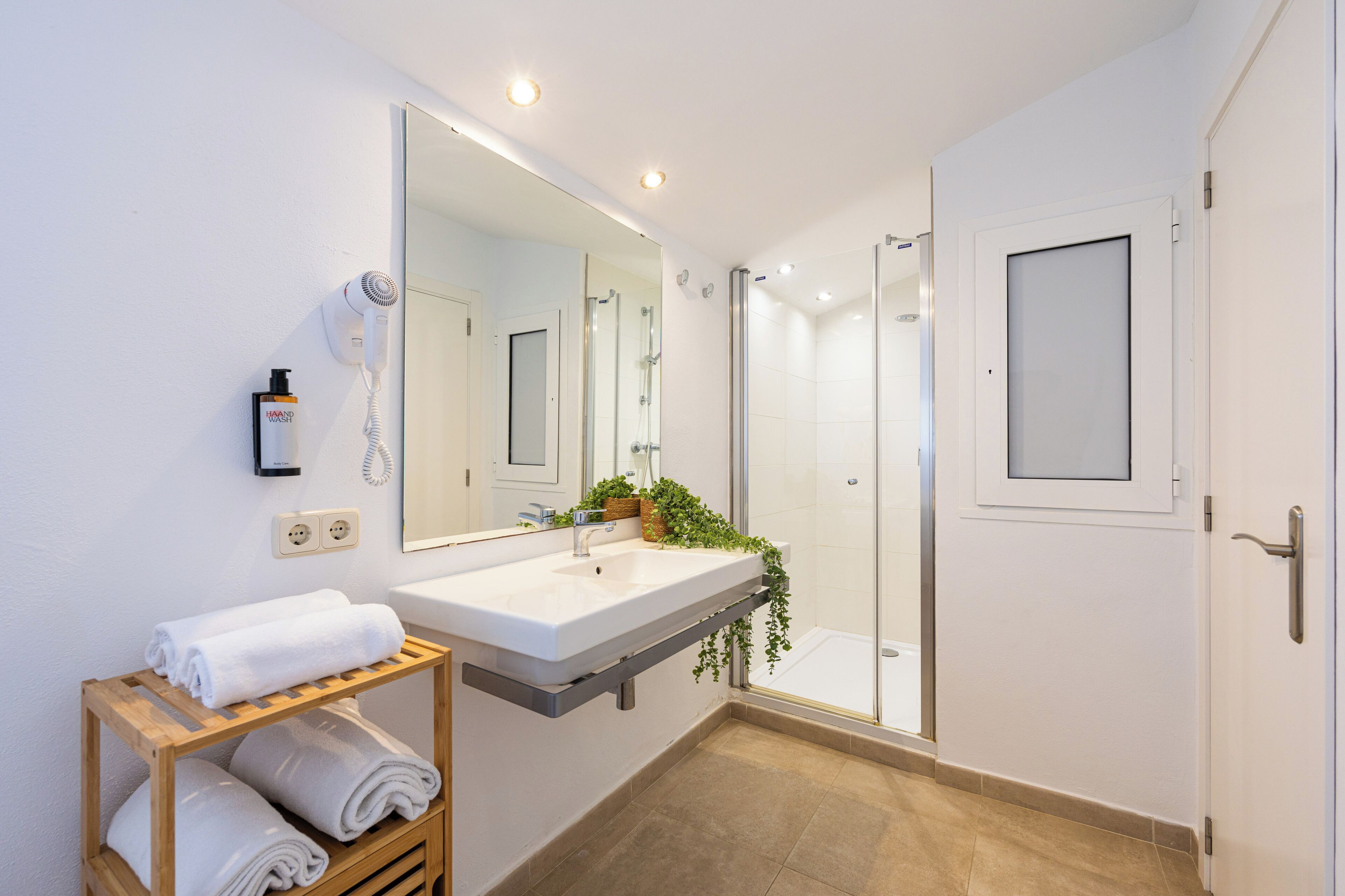 Une salle de bain moderne avec un grand miroir, un lavabo, un sèche-cheveux et une douche.