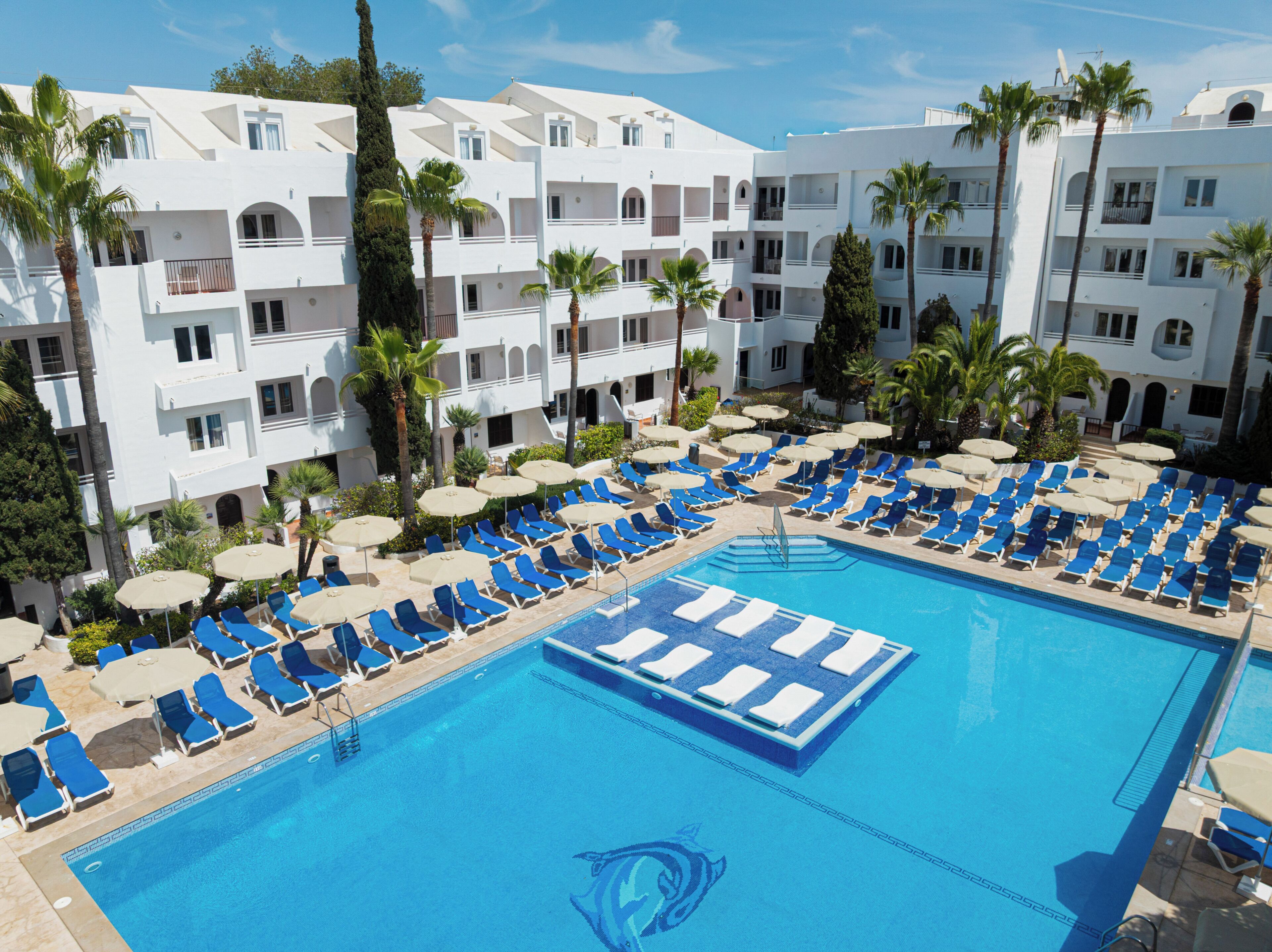 Ein Hotel mit Swimmingpool, umgeben von blauen Liegestühlen und Palmen.