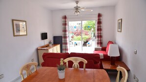 A dining area with a wooden table and chairs, a small potted plant, and a red sofa.