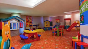 Espaço infantil com diferentes estruturas de recreação, um escorrega e uma mesa.