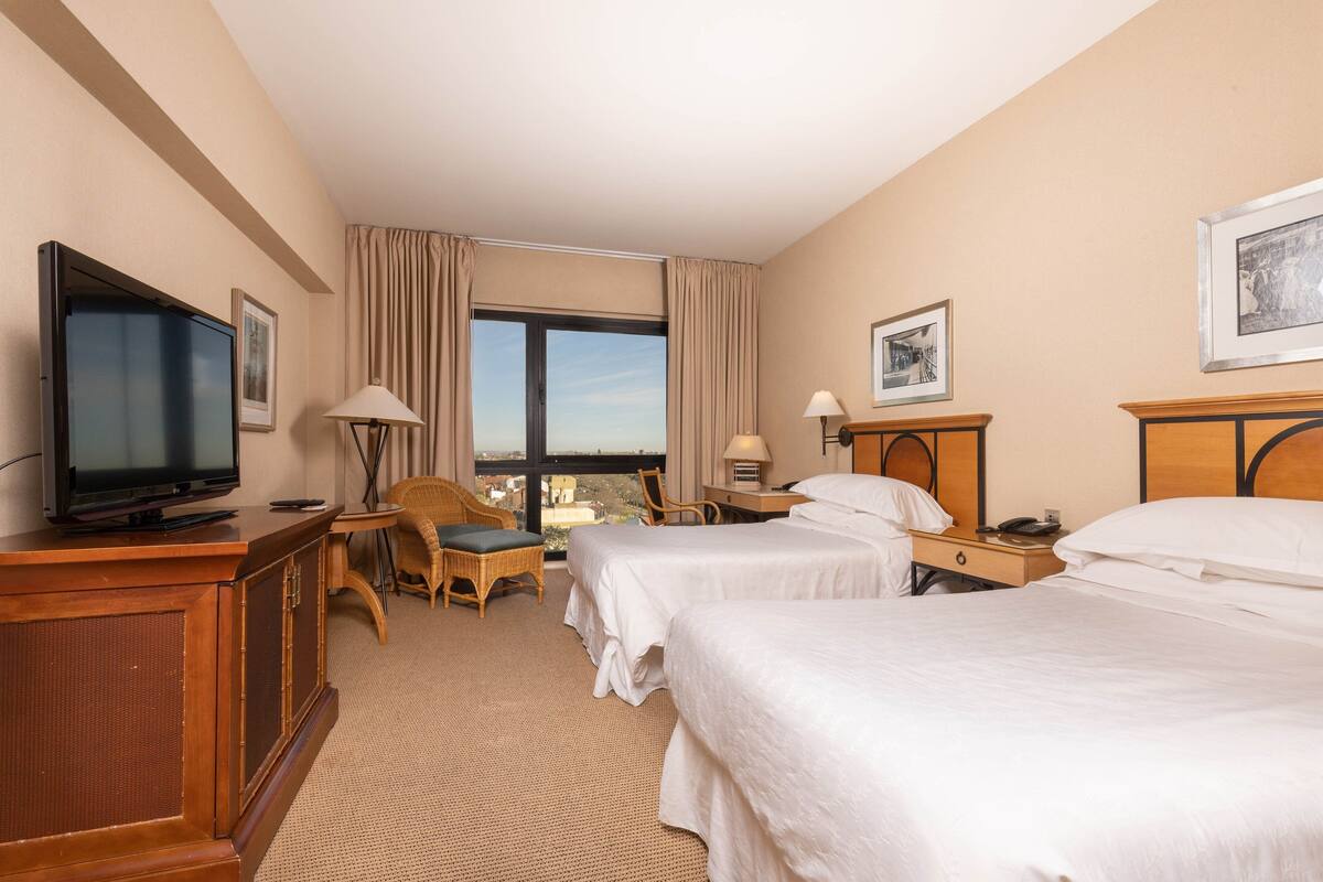 Une chambre d’hôtel avec deux lits, une télévision, un bureau, une chaise et une grande fenêtre.