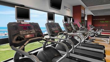 A gym with treadmills and exercise equipment, large windows with a view of the ocean, and motivational wall quotes.
