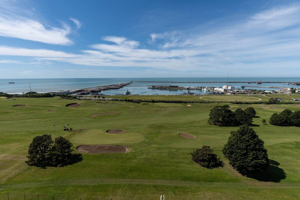Un parcours de golf agrémenté de bunkers, d’arbres et offrant une vue sur la mer et le port.