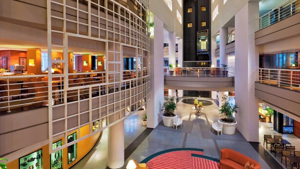 Eine mehrstöckige Hotelhalle mit einem zentralen Atrium, Sitzbereichen und Blumentöpfen.