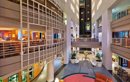 A multi-level hotel lobby with a central atrium, seating areas, and potted plants.