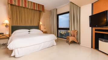 Quarto de hotel com uma cama grande, televisão, cadeira e janela com vista para a cidade.