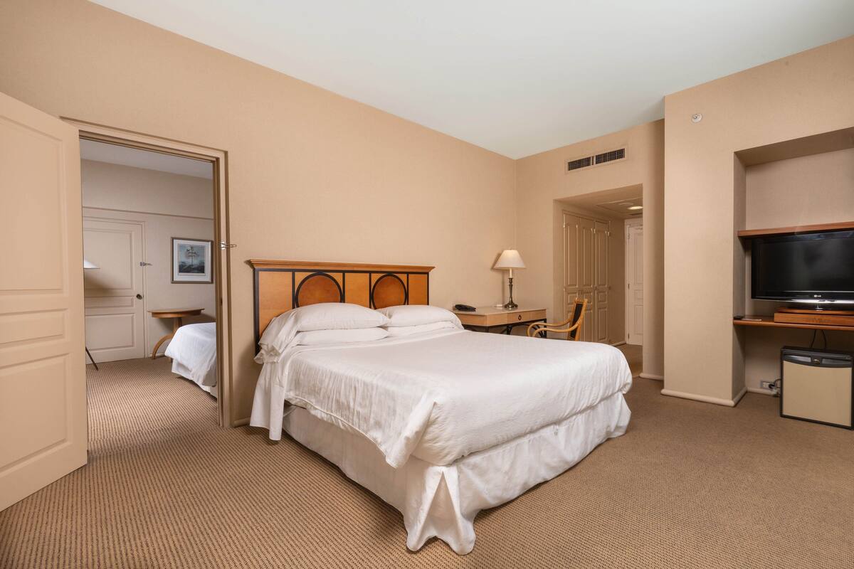 Une chambre d’hôtel comprenant un lit, un bureau, une chaise, une télévision et une porte donnant sur une autre pièce.