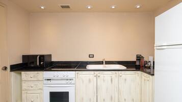 A kitchen with white cabinets, a black countertop, a microwave, a stove, and a sink.