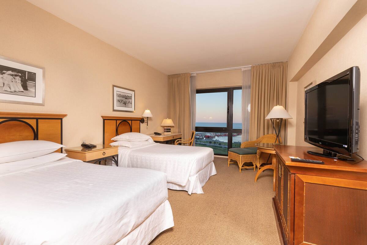 Une chambre d’hôtel avec deux lits, une télévision, un bureau avec une lampe et une chaise.