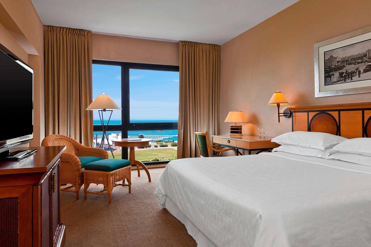 Une chambre d’hôtel équipée d’un lit, d’un bureau, d’une chaise, d’une télévision et offrant une vue sur l’océan.