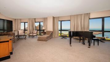 Une chambre d’hôtel spacieuse dotée d’un grand téléviseur à écran plat, d’un piano, d’un canapé et offrant une vue sur la ville et l’eau.