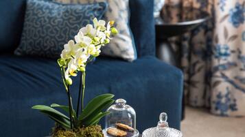 Una stanza con un divano blu, cuscini decorati, un vaso bianco con un'orchidea, un portacandela di vetro e un tavolino.