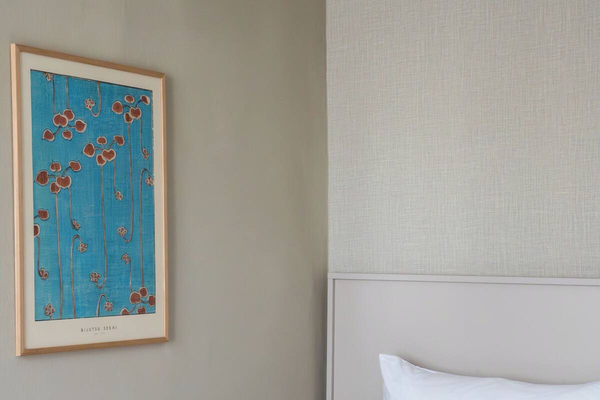 Un letto rifatto con cura, coperto da biancheria bianca e azzurra, un quadro incorniciato appeso alla parete e un pannello murale con texture.
