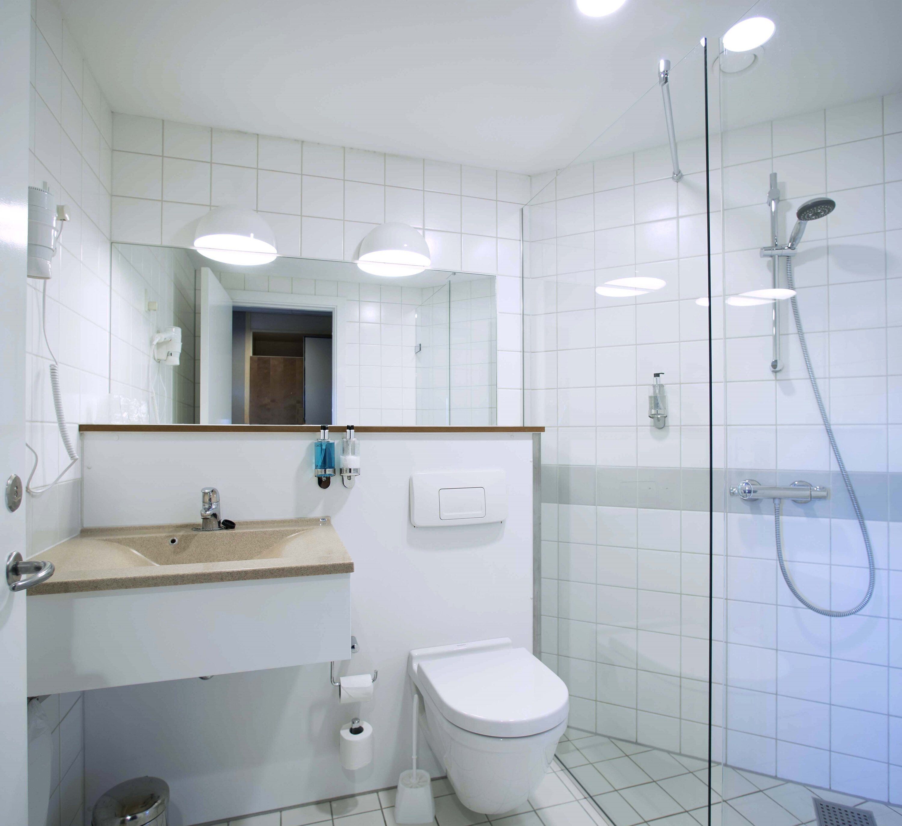 Un baño moderno con lavabo, espejo, inodoro y ducha.