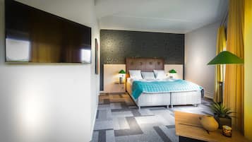 Quarto de hotel moderno com uma cama grande, televisão de tela plana, escrivaninha com abajur e uma planta em vaso.