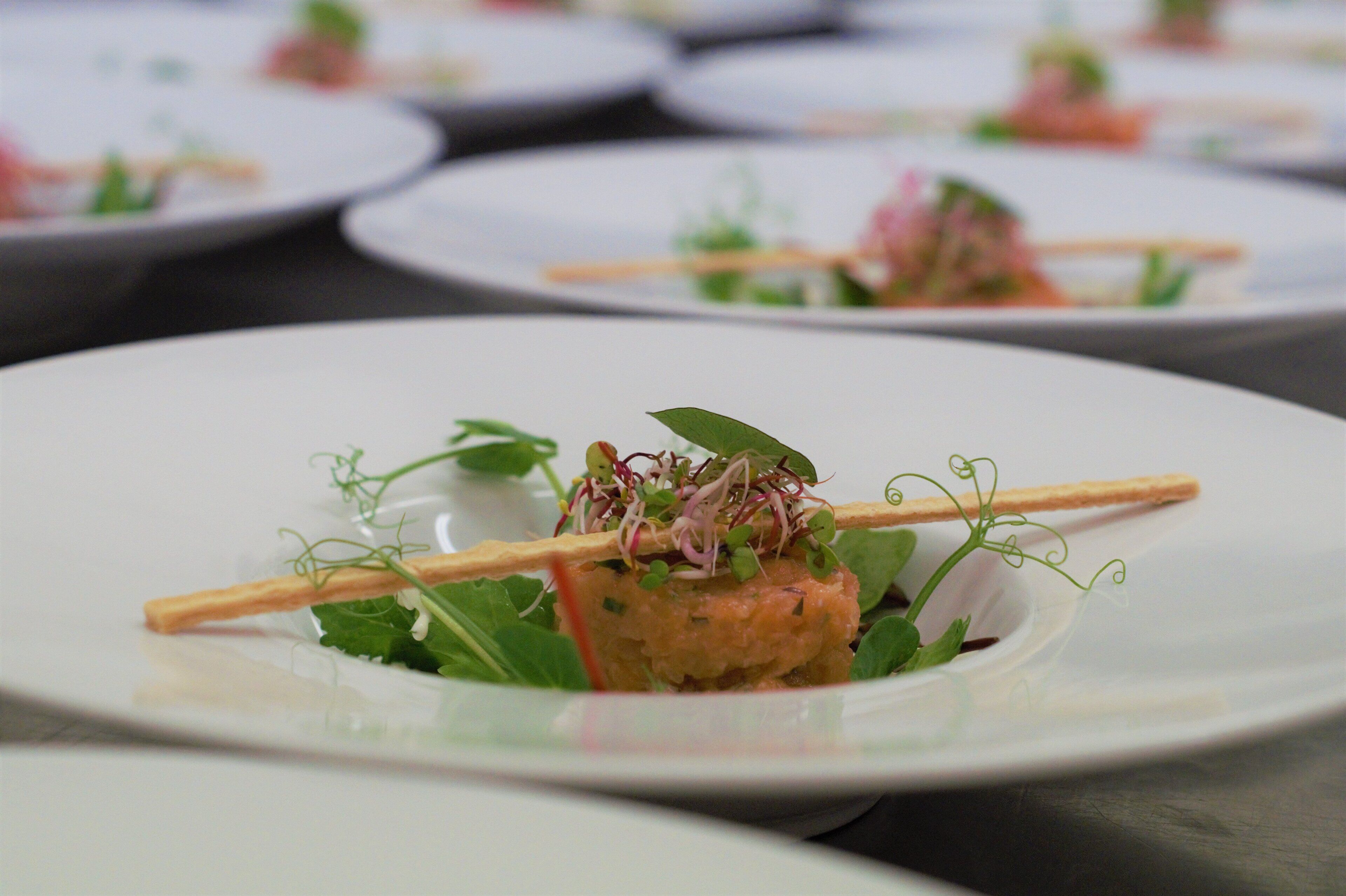 A series of white plates with a central dish of food garnished with greens and a crispy element, possibly a cracker, on a table.
