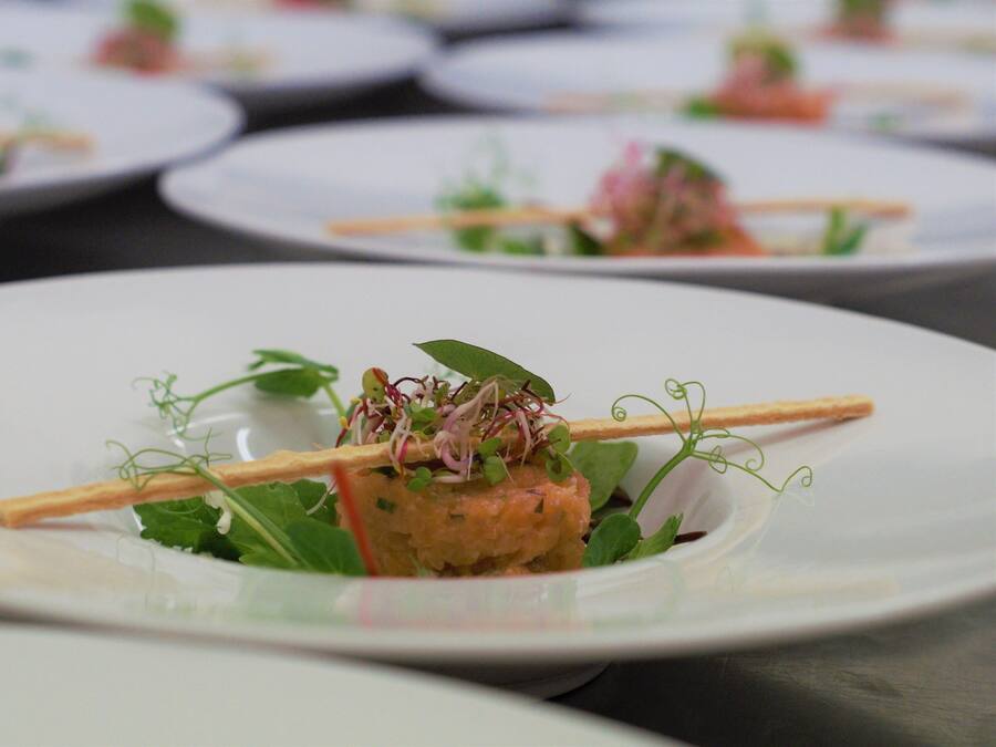 A series of white plates with a central dish of food garnished with greens and a crispy element, possibly a cracker, on a table.