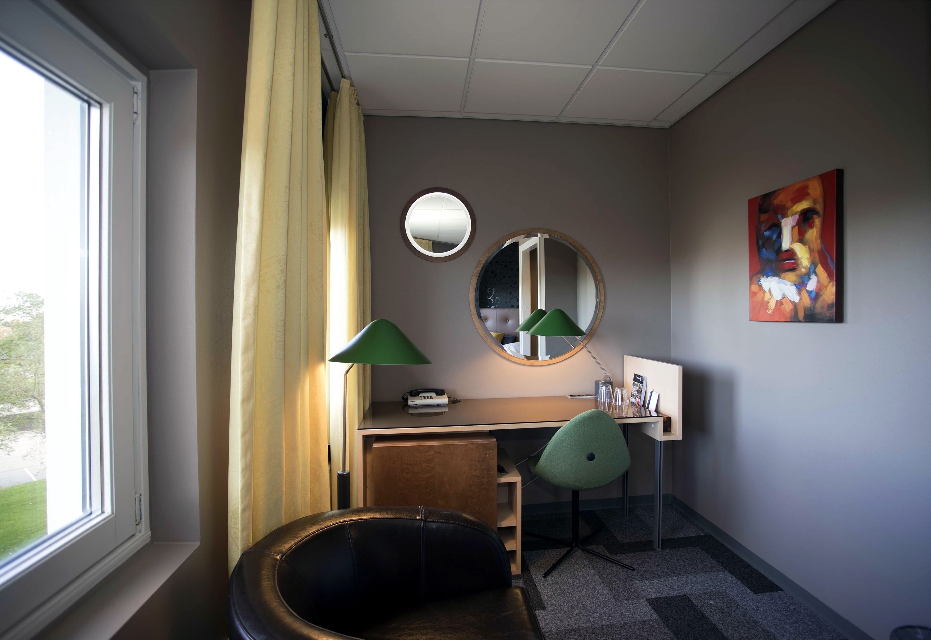 Ein Hotelzimmer mit Schreibtisch, zwei Stühlen, einem runden Spiegel und einem Gemälde an der Wand.