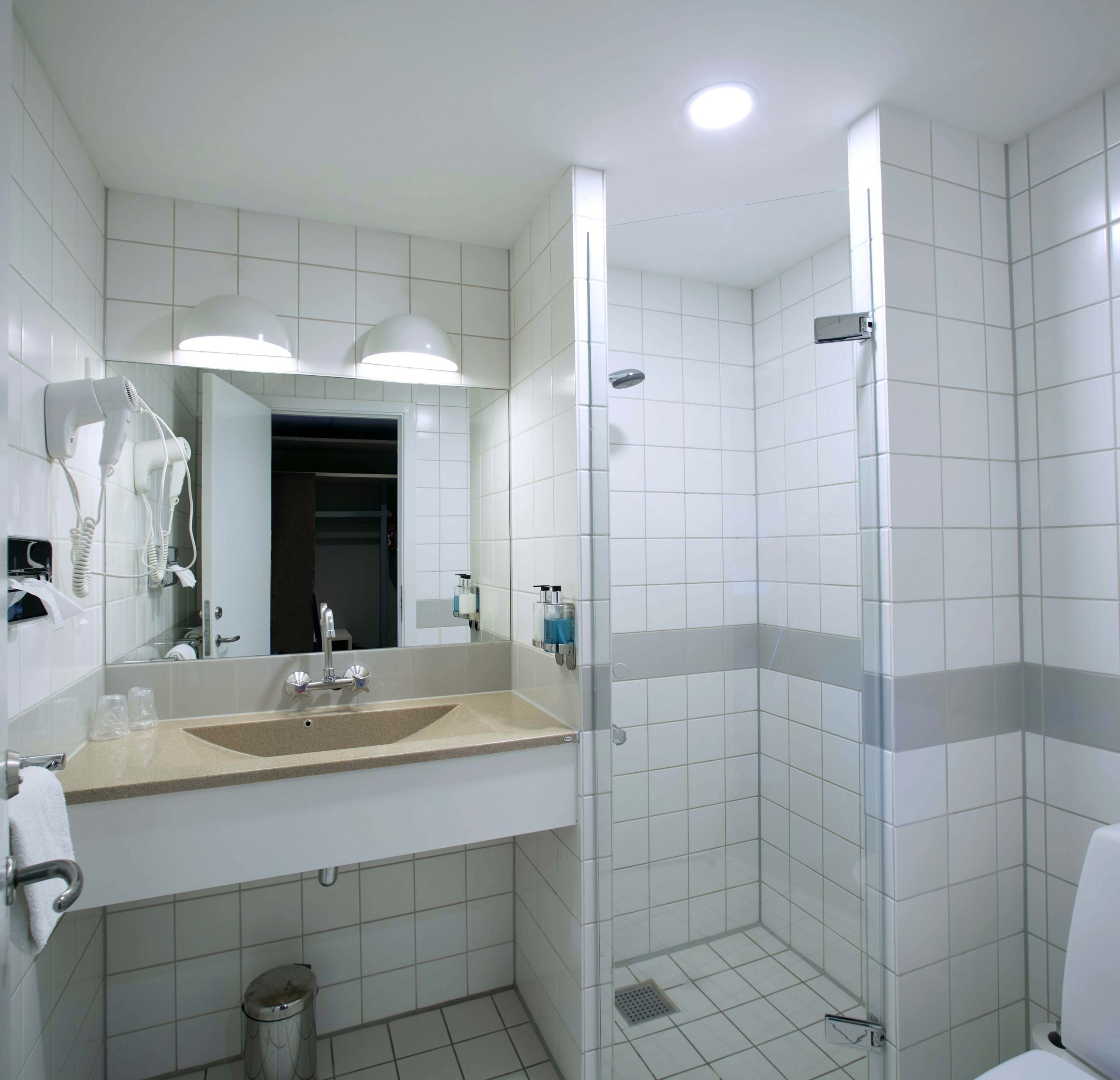 A modern bathroom with a sink, mirror, hair dryer, and shower.