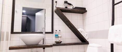 A bathroom with a white sink, a large mirror, and a wooden shelf.