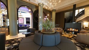A modern lounge area with a central seating arrangement, a fireplace, and a decorative plant. - Lumière Boutiquehotel im Fürstenhof Leipzig (Leipzig)