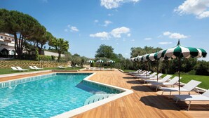 A swimming pool with a wooden deck, lounge chairs, and umbrellas.