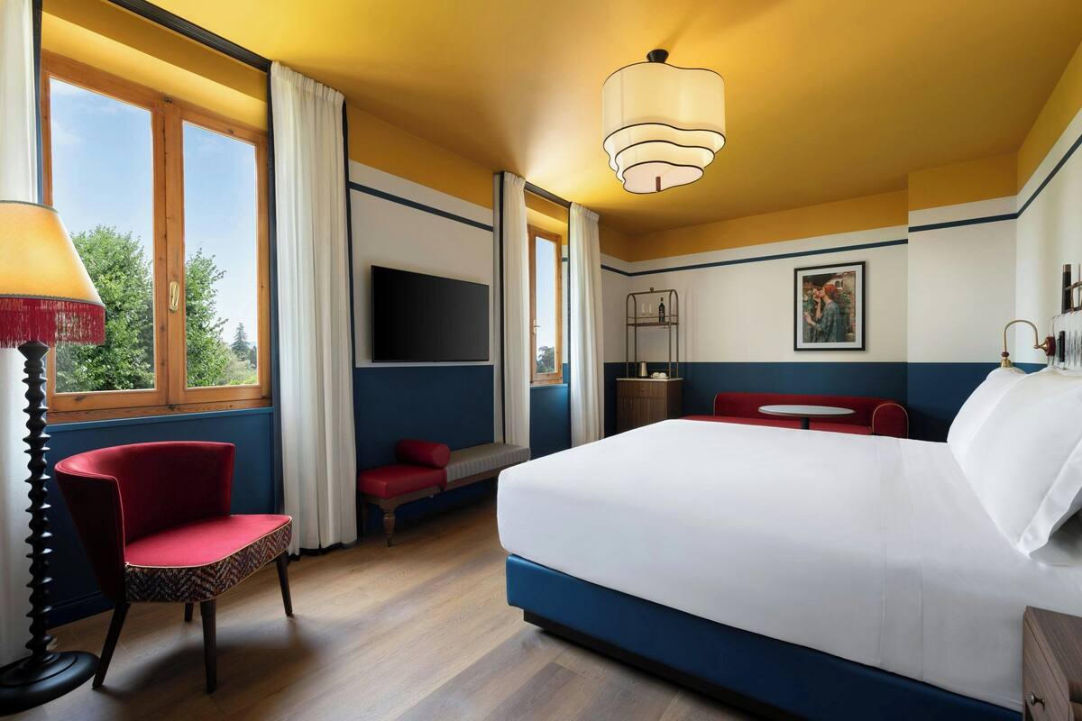 A hotel room with a large bed, a red chair, a small table, and a TV.